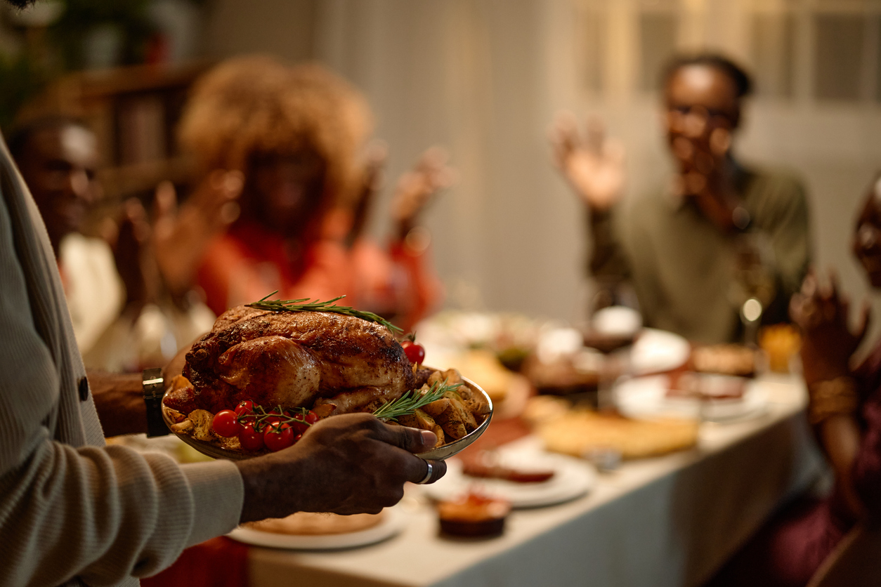 African American man holding roasted turkey platter during Thanksgiving dinner with family.