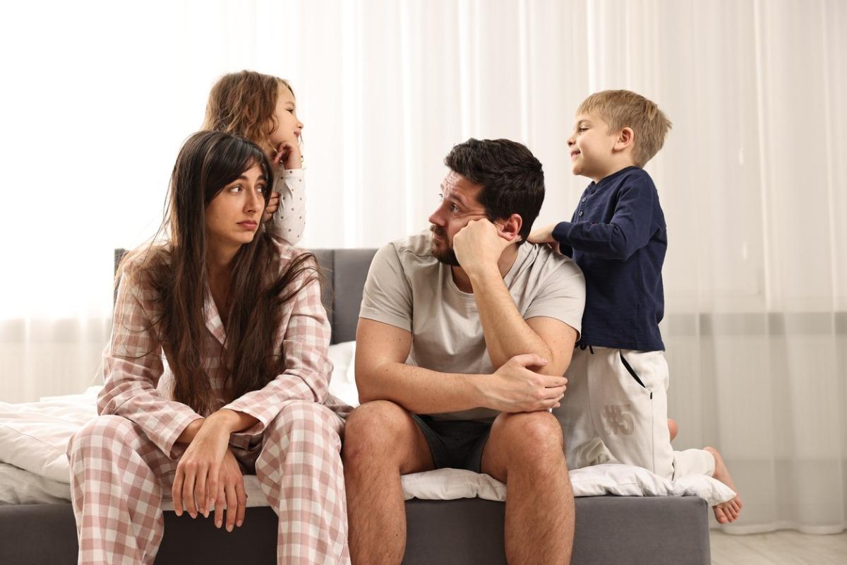 Two parents looking frustrated from being in a small hotel room with two young kids.